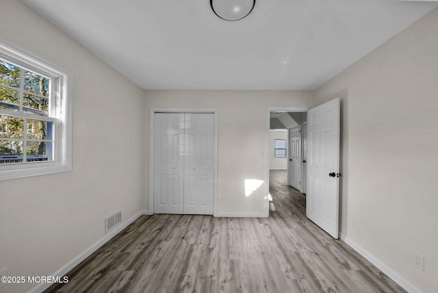 unfurnished bedroom with wood finished floors, visible vents, a closet, and baseboards