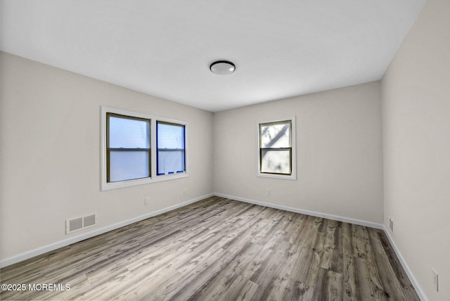 unfurnished room featuring wood finished floors, visible vents, and baseboards