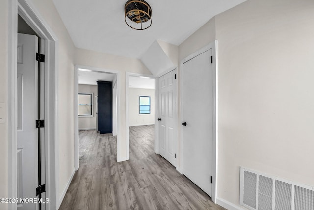 corridor with light wood finished floors, visible vents, and baseboards