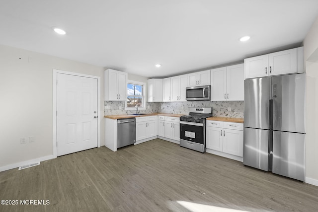 kitchen featuring visible vents, a sink, backsplash, stainless steel appliances, and light wood-style floors