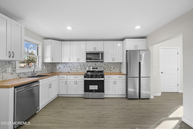 kitchen with light wood-type flooring, appliances with stainless steel finishes, white cabinets, wood counters, and a sink