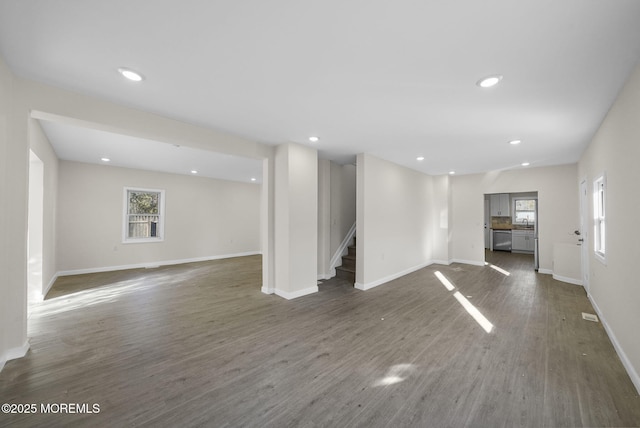 unfurnished living room with stairway, baseboards, dark wood-style flooring, and a wealth of natural light