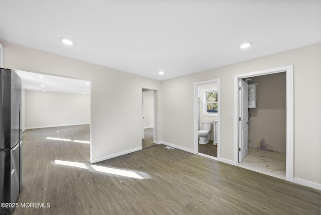 unfurnished bedroom featuring a walk in closet, baseboards, recessed lighting, freestanding refrigerator, and wood finished floors