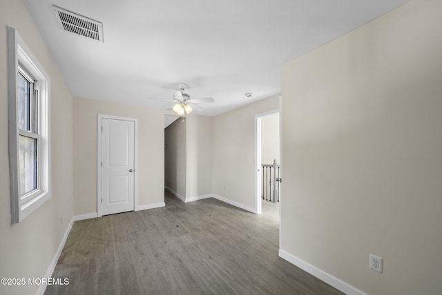 empty room with ceiling fan, visible vents, baseboards, and wood finished floors