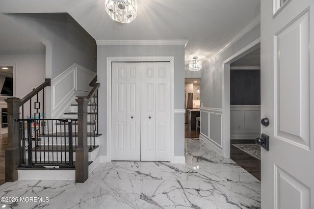 entryway featuring crown molding, a decorative wall, a notable chandelier, and marble finish floor