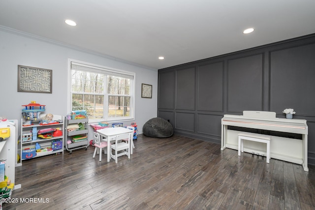 rec room featuring crown molding, a decorative wall, recessed lighting, and wood finished floors