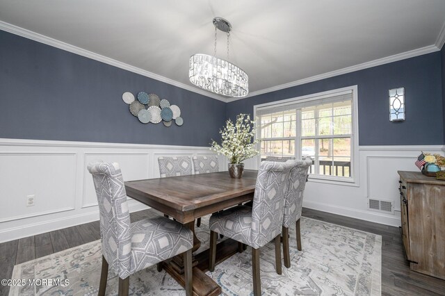 dining space with visible vents, a wainscoted wall, ornamental molding, wood finished floors, and a chandelier