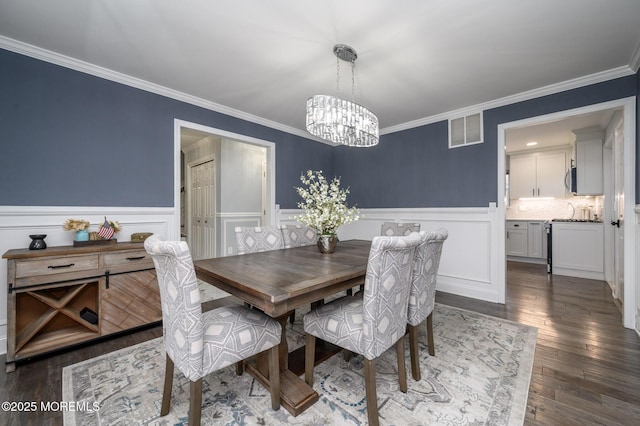 dining room featuring a wainscoted wall, visible vents, ornamental molding, dark wood-type flooring, and a notable chandelier