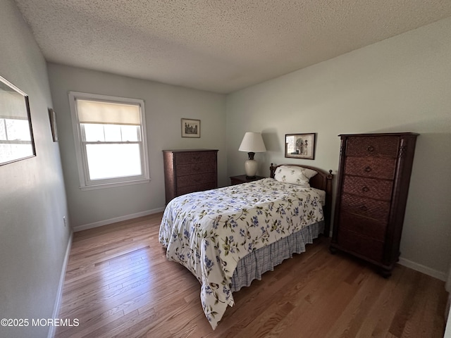 bedroom featuring a textured ceiling, baseboards, and wood finished floors