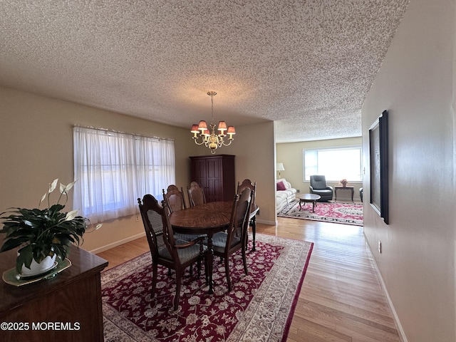 dining area with baseboards, a textured ceiling, light wood-type flooring, and an inviting chandelier