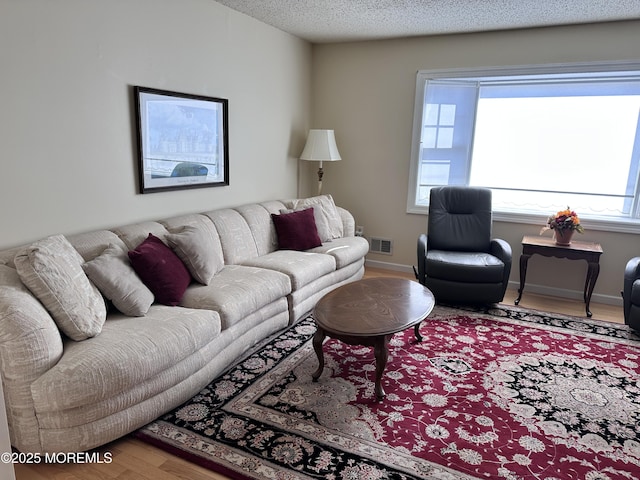 living room with visible vents, a textured ceiling, baseboards, and wood finished floors