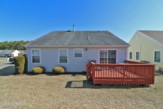 back of house with a lawn, a wooden deck, and roof with shingles