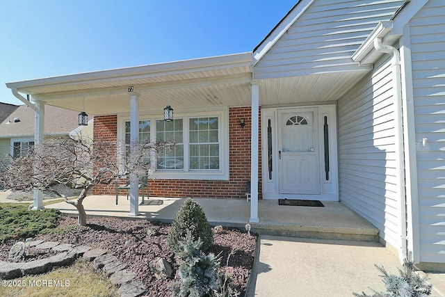 doorway to property featuring brick siding and a porch