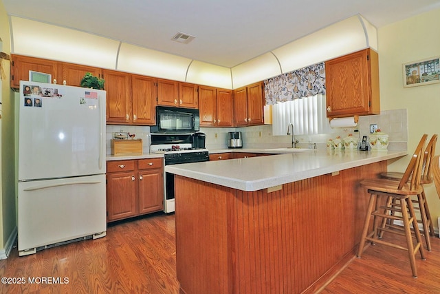 kitchen featuring a sink, freestanding refrigerator, gas stove, black microwave, and light countertops