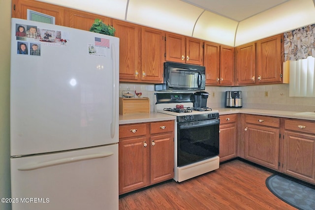 kitchen with black microwave, light countertops, range with gas stovetop, freestanding refrigerator, and dark wood-style floors