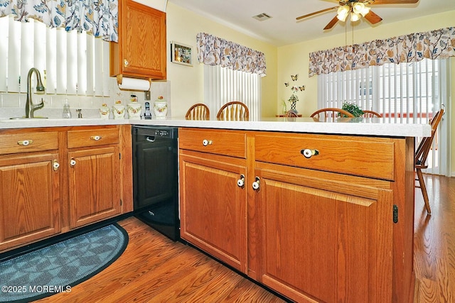 kitchen featuring a peninsula, brown cabinetry, black dishwasher, and light countertops