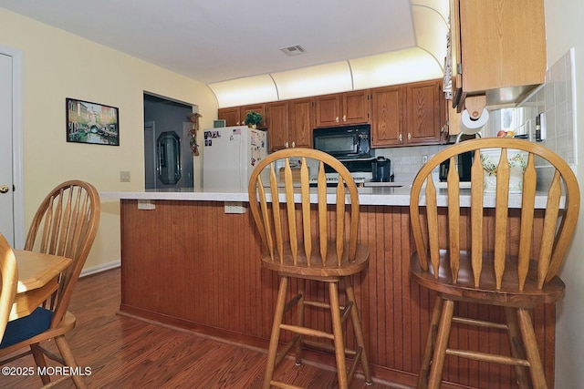 kitchen featuring dark wood-type flooring, freestanding refrigerator, brown cabinetry, light countertops, and black microwave