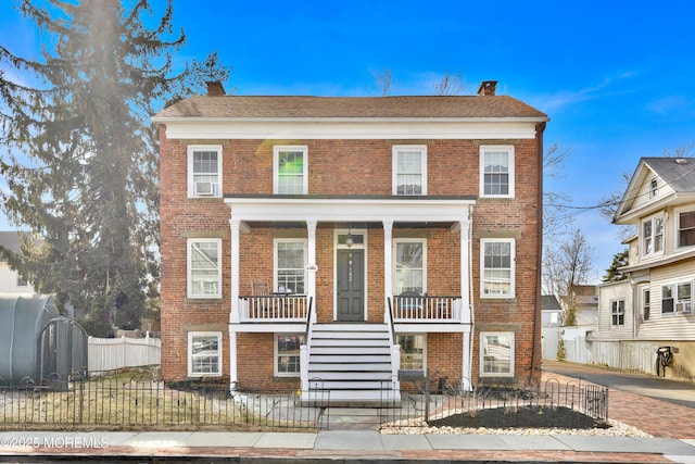 view of front of property with a porch, brick siding, a fenced front yard, and a chimney