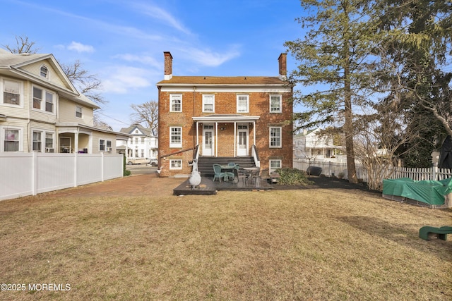 back of house featuring brick siding, a fenced backyard, a chimney, and a lawn