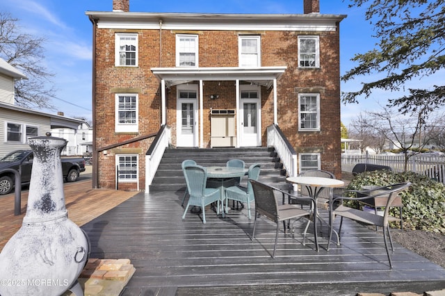 rear view of house featuring outdoor dining area, brick siding, a chimney, and fence