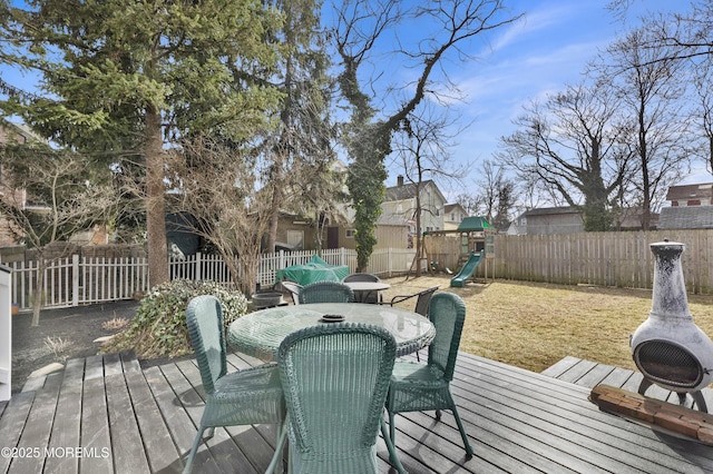 deck with a playground, outdoor dining area, a fenced backyard, and a yard