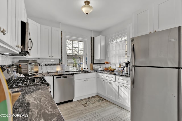 kitchen featuring dark stone countertops, a sink, decorative backsplash, white cabinets, and appliances with stainless steel finishes