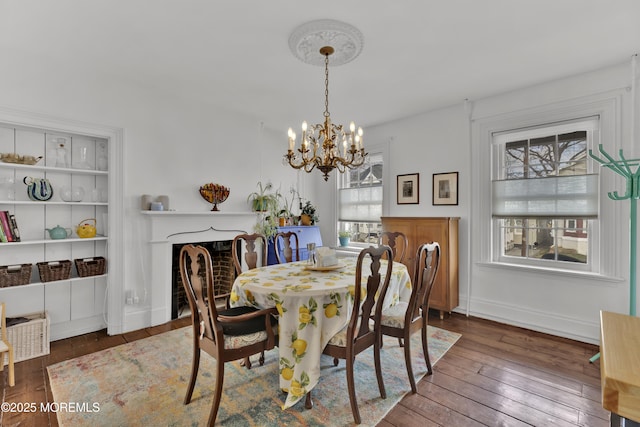 dining room with baseboards, wood-type flooring, a chandelier, and a fireplace