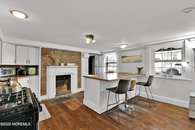 kitchen featuring a fireplace with flush hearth, a healthy amount of sunlight, freestanding refrigerator, and dark wood-style flooring