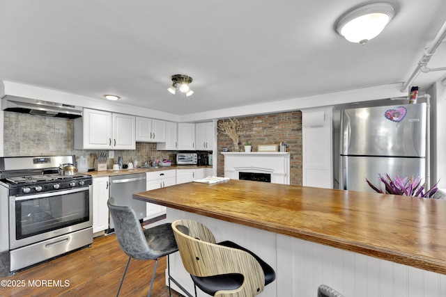 kitchen with dark wood finished floors, butcher block counters, a kitchen bar, range hood, and appliances with stainless steel finishes