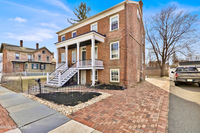 view of front of property with driveway, a fenced front yard, a porch, brick siding, and stairs