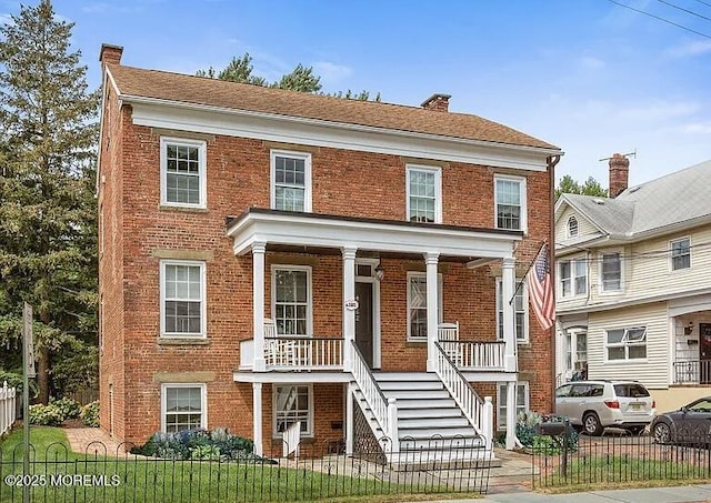 view of front of house with brick siding, a fenced front yard, stairway, covered porch, and a chimney