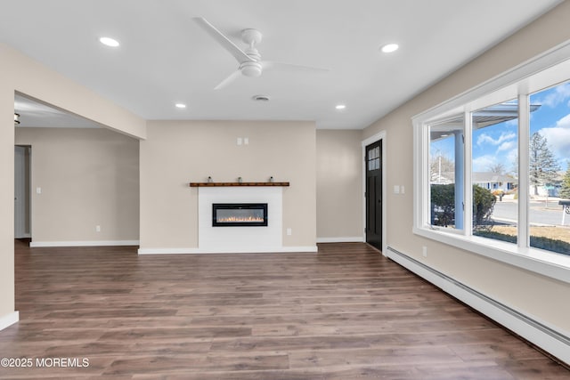 unfurnished living room featuring a glass covered fireplace, recessed lighting, a baseboard heating unit, and wood finished floors