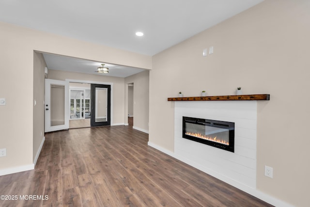 unfurnished living room with a glass covered fireplace, dark wood-type flooring, and baseboards