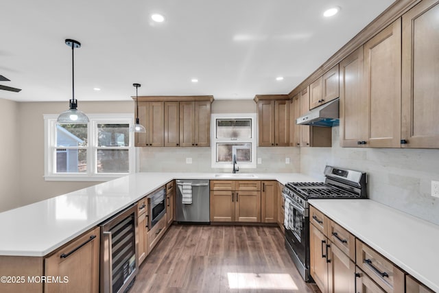 kitchen featuring under cabinet range hood, a sink, wine cooler, appliances with stainless steel finishes, and a peninsula