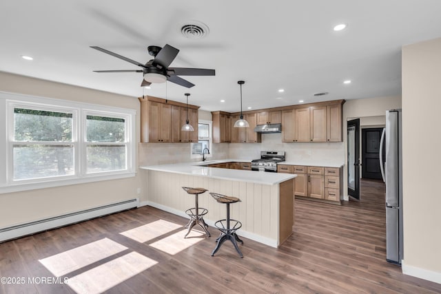 kitchen with visible vents, a baseboard heating unit, under cabinet range hood, appliances with stainless steel finishes, and a peninsula