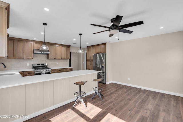 kitchen with dark wood-type flooring, range hood, appliances with stainless steel finishes, a peninsula, and a sink