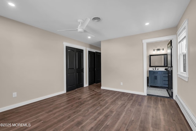 unfurnished bedroom with visible vents, multiple closets, a baseboard heating unit, dark wood finished floors, and baseboards