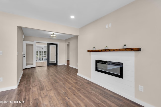 unfurnished living room with dark wood-style floors, a glass covered fireplace, and baseboards