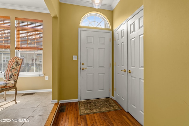 entryway with light wood-type flooring, visible vents, baseboards, and ornamental molding