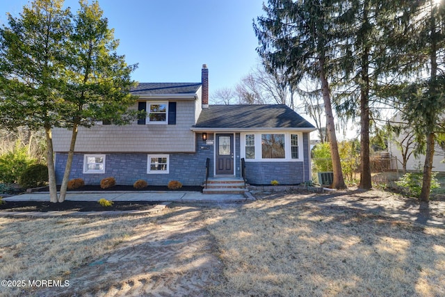 tri-level home featuring central air condition unit, stone siding, and a chimney