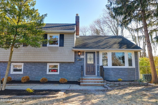 view of front facade featuring central AC unit, roof with shingles, and a chimney