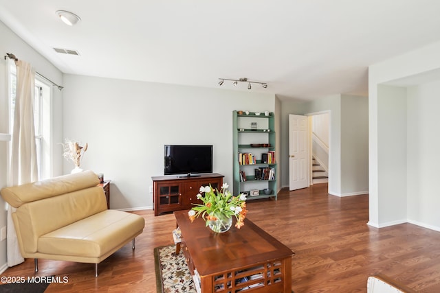 living area featuring baseboards, wood finished floors, visible vents, and stairs
