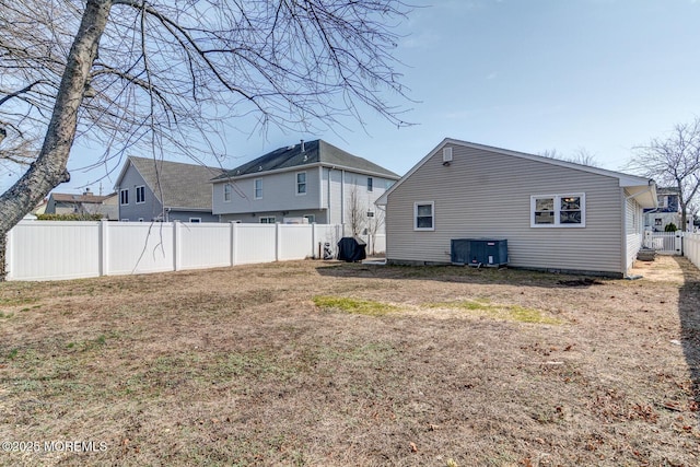 rear view of house featuring cooling unit, a lawn, and a fenced backyard