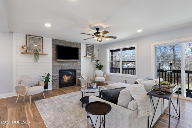 living area with a ceiling fan, wood finished floors, recessed lighting, a stone fireplace, and baseboards