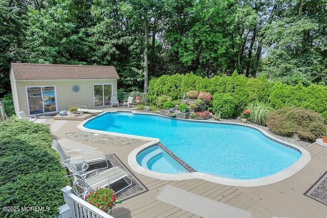 view of swimming pool featuring a deck, a pool with connected hot tub, an outdoor structure, and a diving board