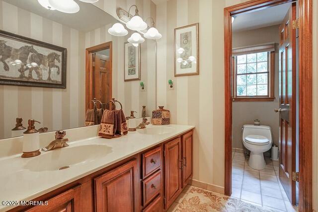 bathroom featuring double vanity, toilet, wallpapered walls, and a sink