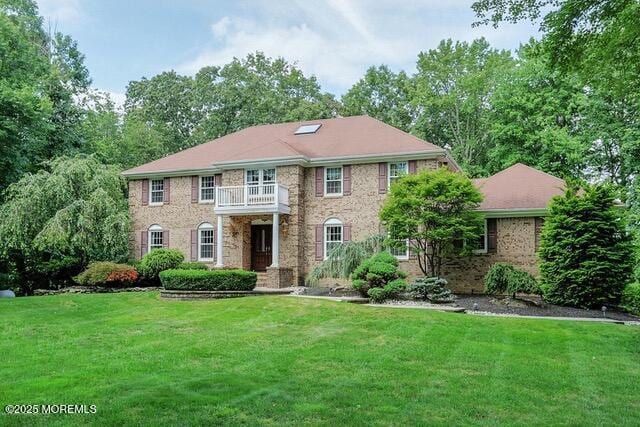 view of front of home featuring brick siding, a balcony, and a front lawn