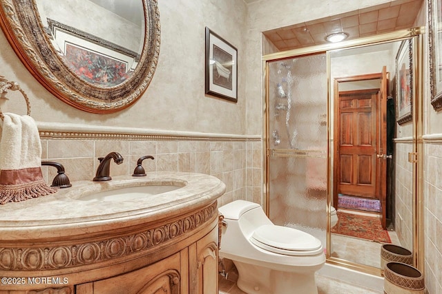 bathroom with a wainscoted wall, toilet, vanity, a stall shower, and tile walls