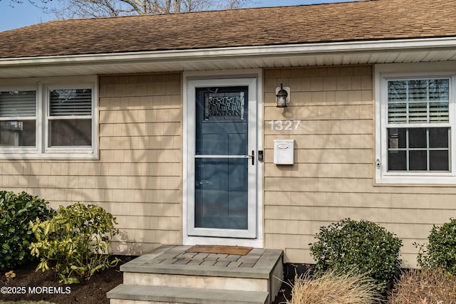 view of exterior entry with roof with shingles