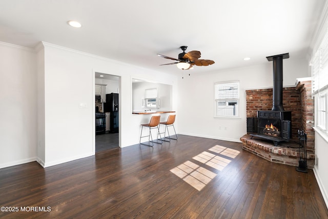 unfurnished living room with baseboards, ceiling fan, ornamental molding, a wood stove, and hardwood / wood-style flooring